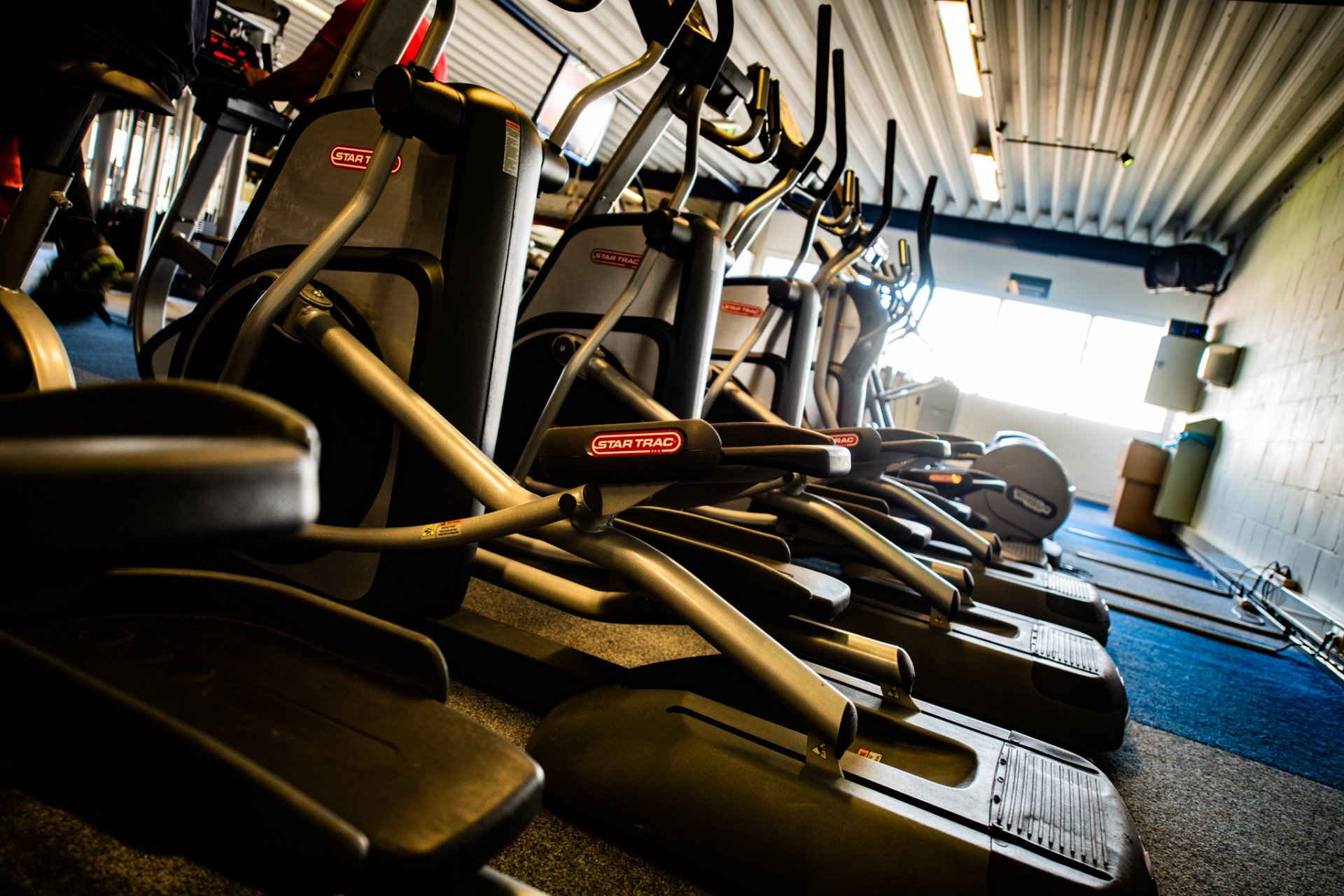 In een sportschool staat een rij elliptische trainers opgesteld.