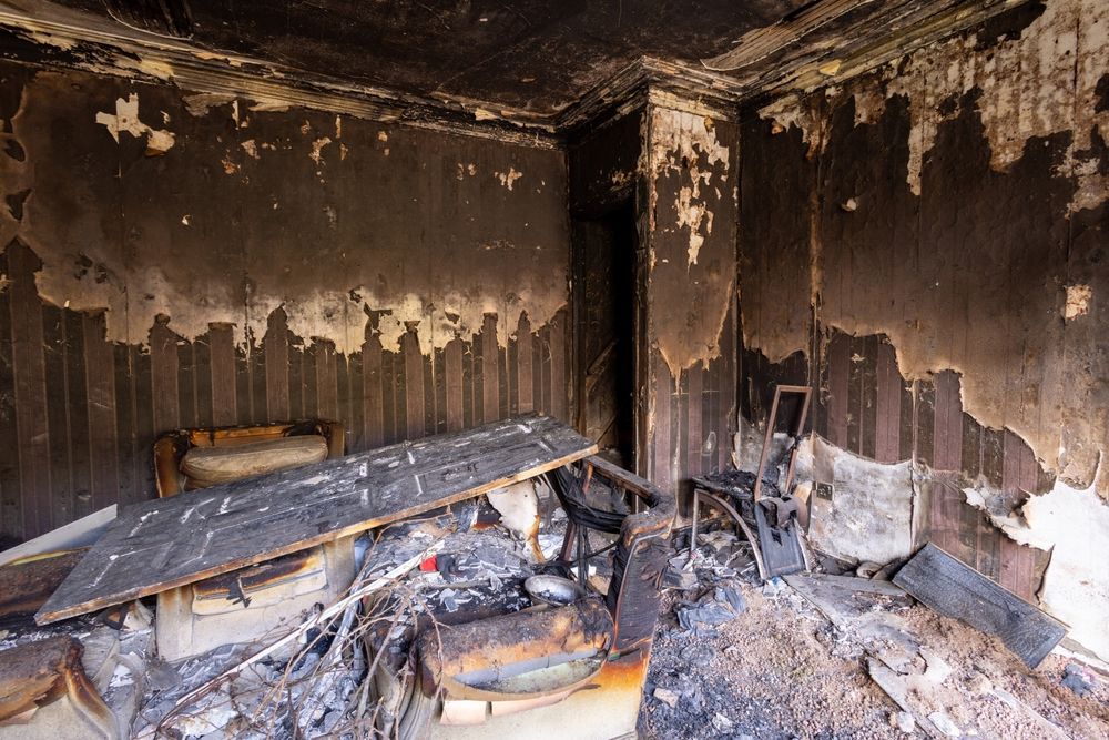 A charred interior room showing severe fire damage, with soot-covered walls and debris scattered across the floor.