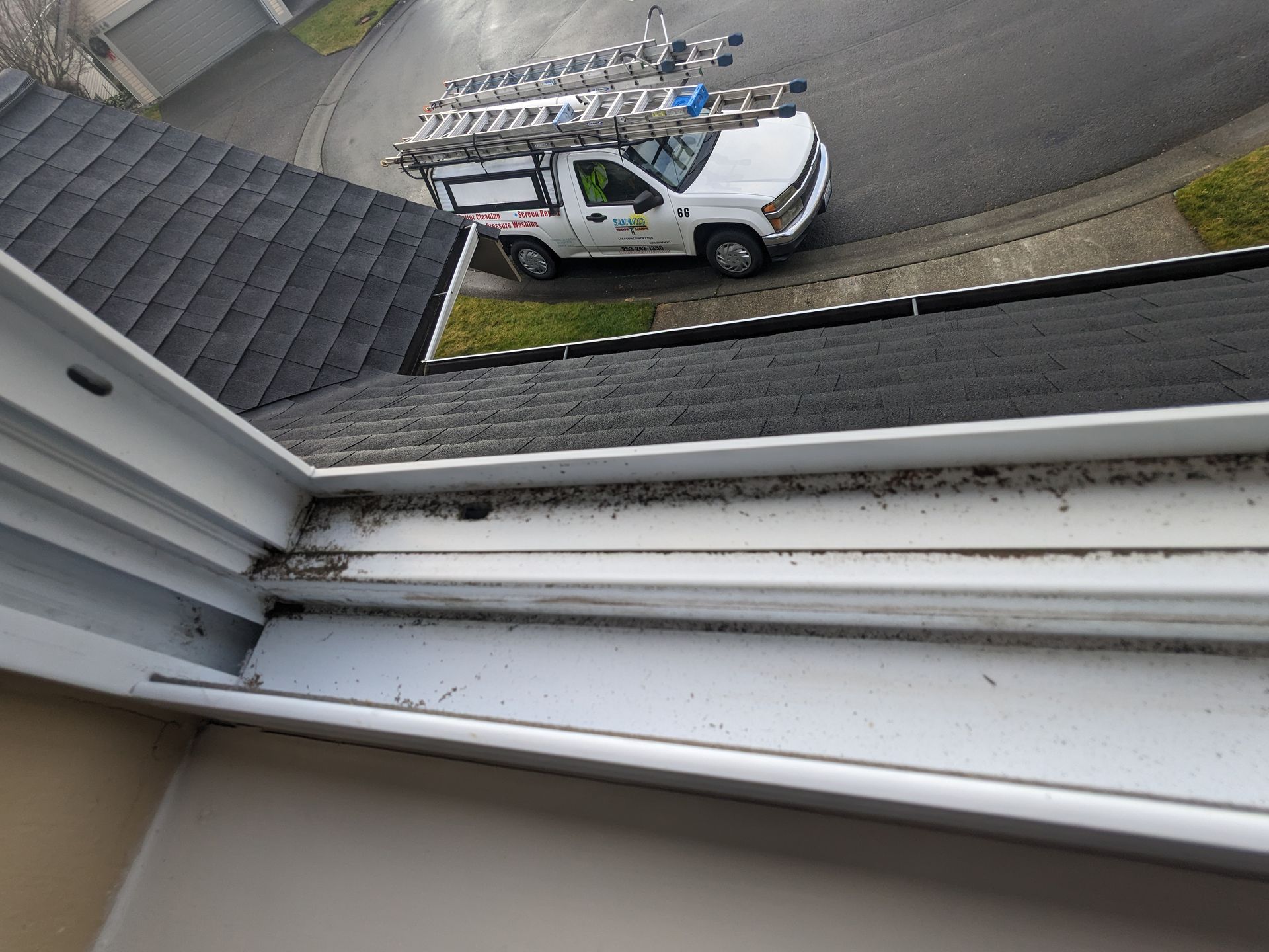 A white truck with a ladder on top of it is parked next to a window.