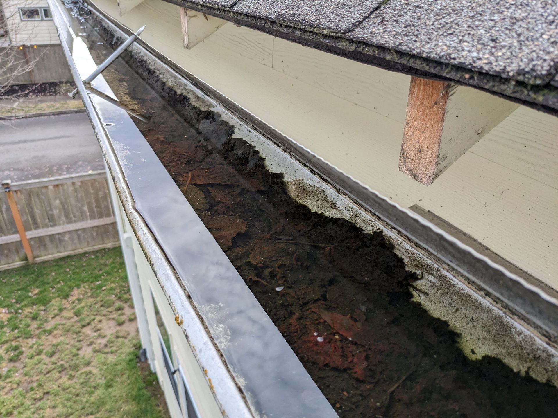 A gutter on the side of a house filled with leaves and dirt.