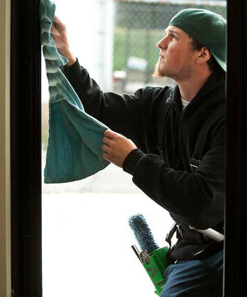 A man in a green hat is cleaning a window with a towel