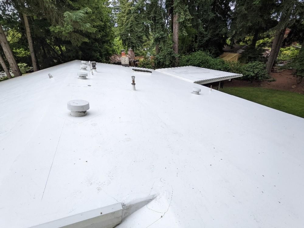 A white roof with a lot of vents and trees in the background.