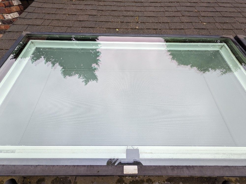 A glass skylight is sitting on top of a brick roof.