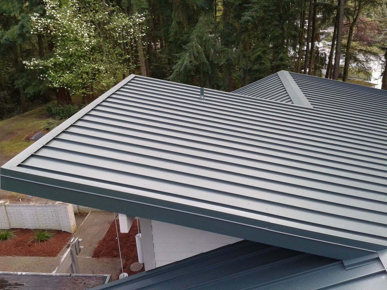 A close up of a gray metal roof with trees in the background