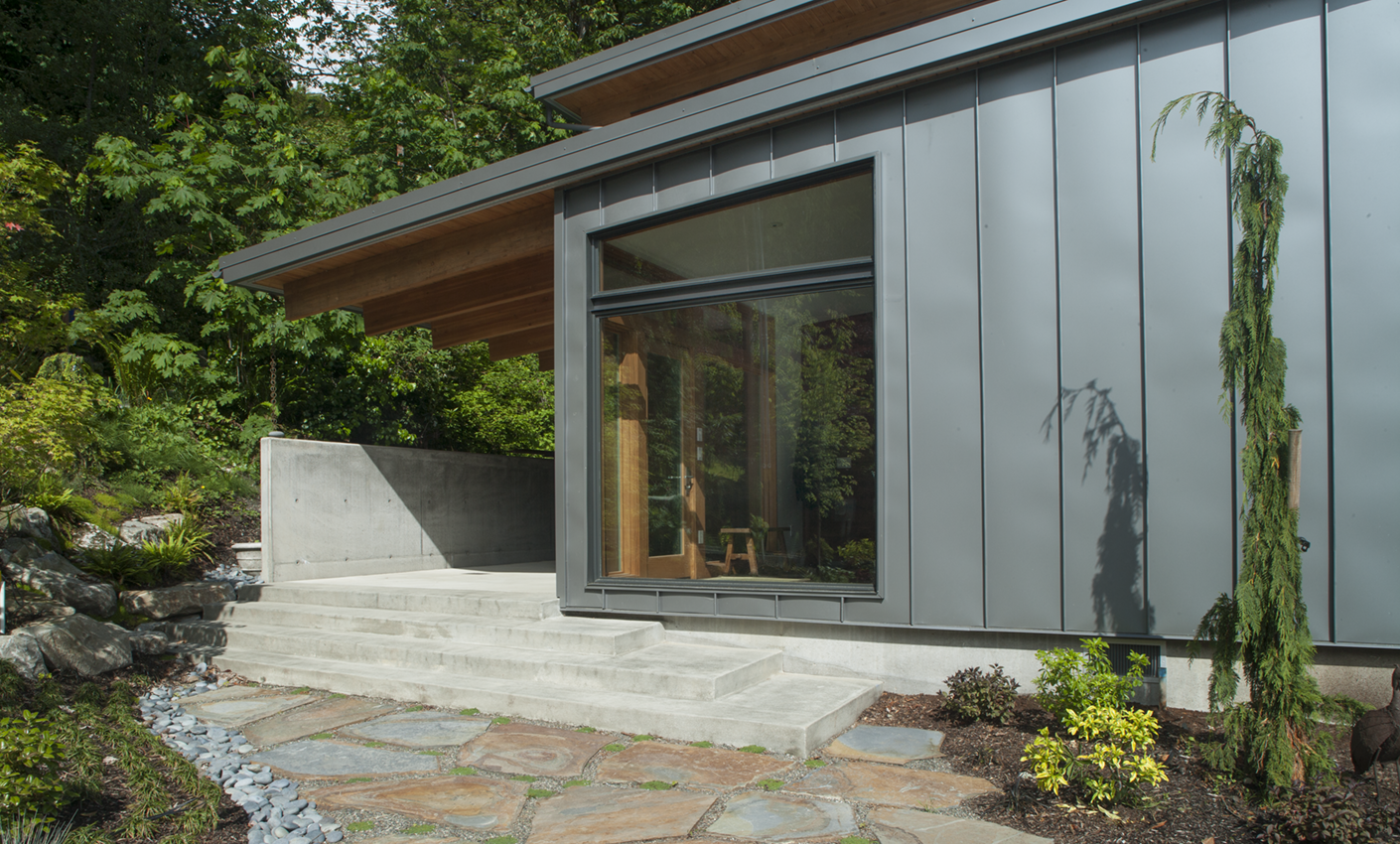 A sleek modern home on Bainbridge Island in Washington Sate resides in a woodsy area, and has gray standing seam metal siding.