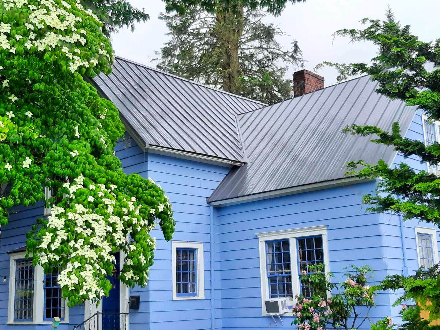 A blue single family home with a gray metal roof. 