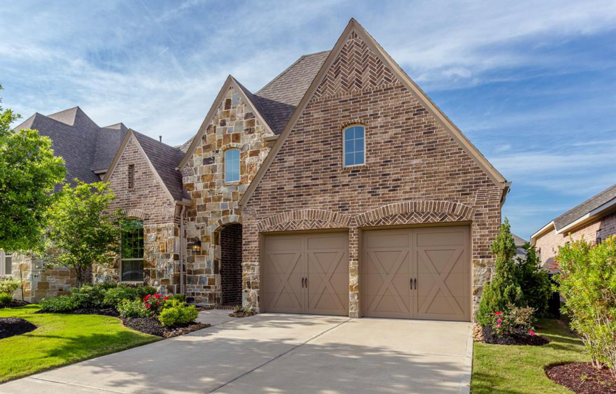 Stone-faced house with two-car garage, tan doors, and driveway.