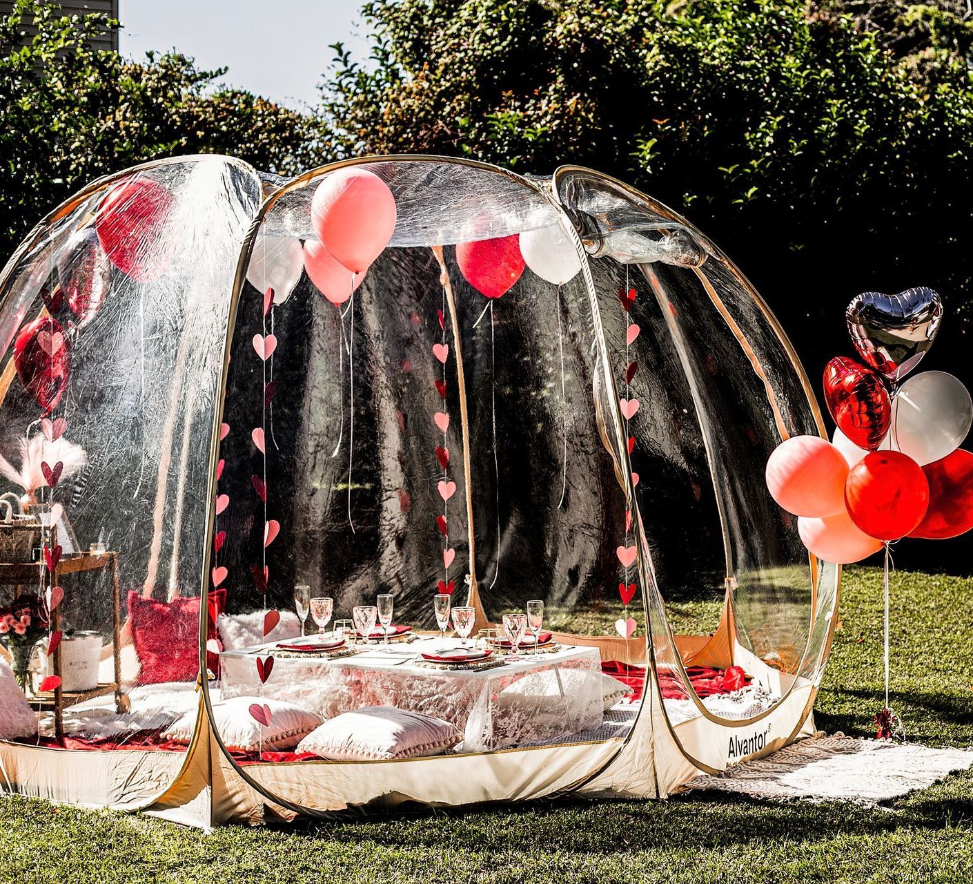 A clear dome with balloons and a table inside of it.