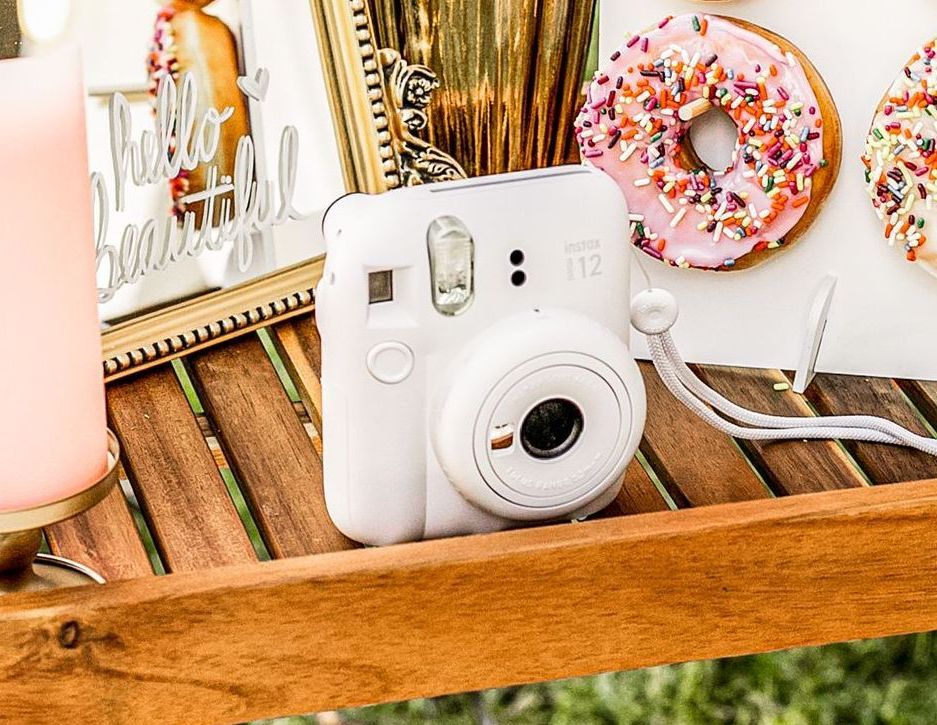 A white camera is sitting on a wooden table next to donuts.