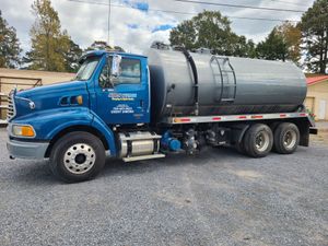 A blue and gray tanker truck is parked in a gravel lot.