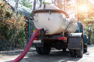 A septic tank truck with a red hose attached to it.