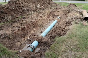 A blue pipe is laying in the dirt next to a pile of dirt.