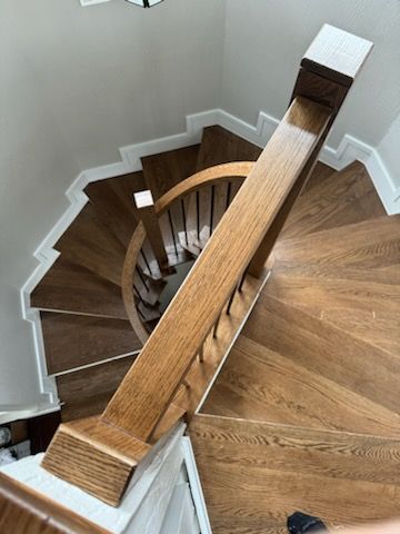 A person is standing on a wooden spiral staircase in a house
