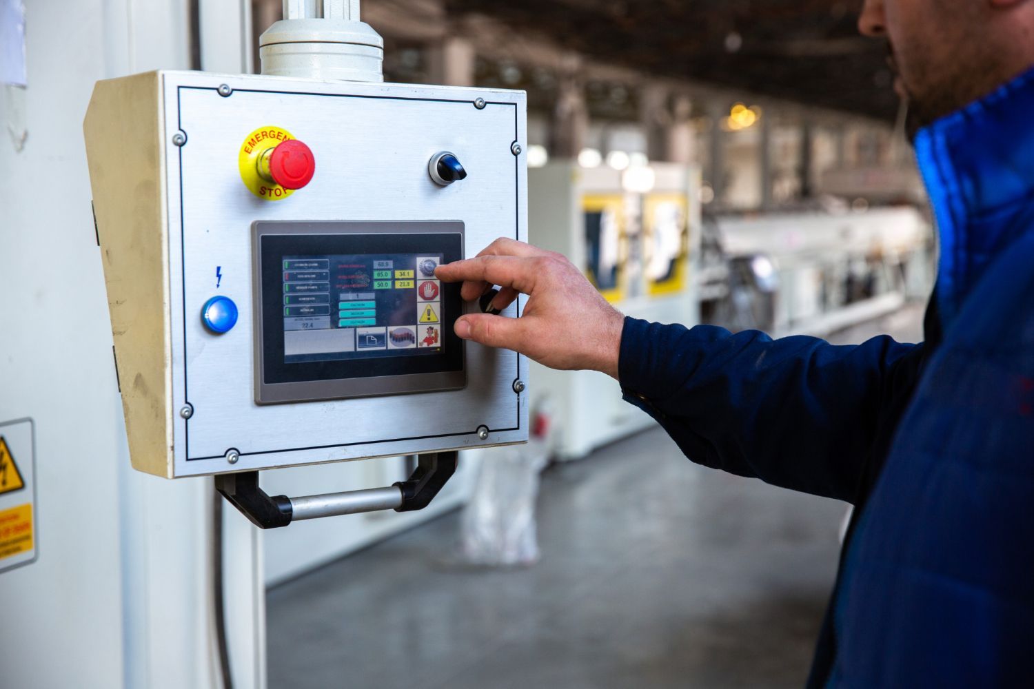 A man is pressing a button on a control panel in a factory.