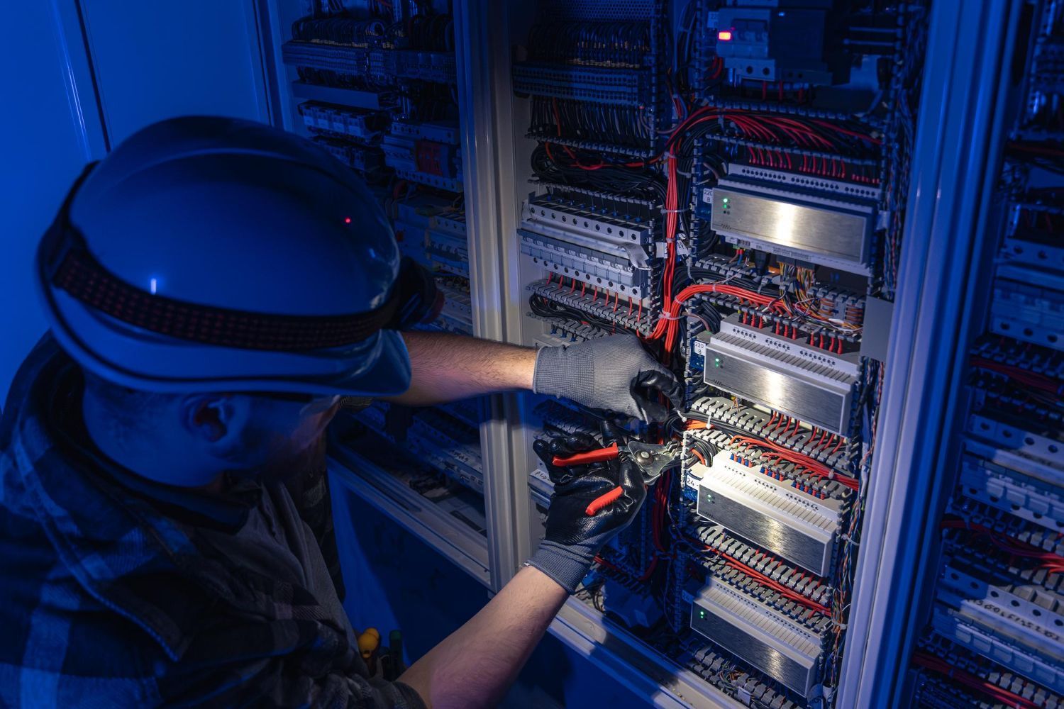 A man wearing a hard hat and gloves is working on an electrical box.