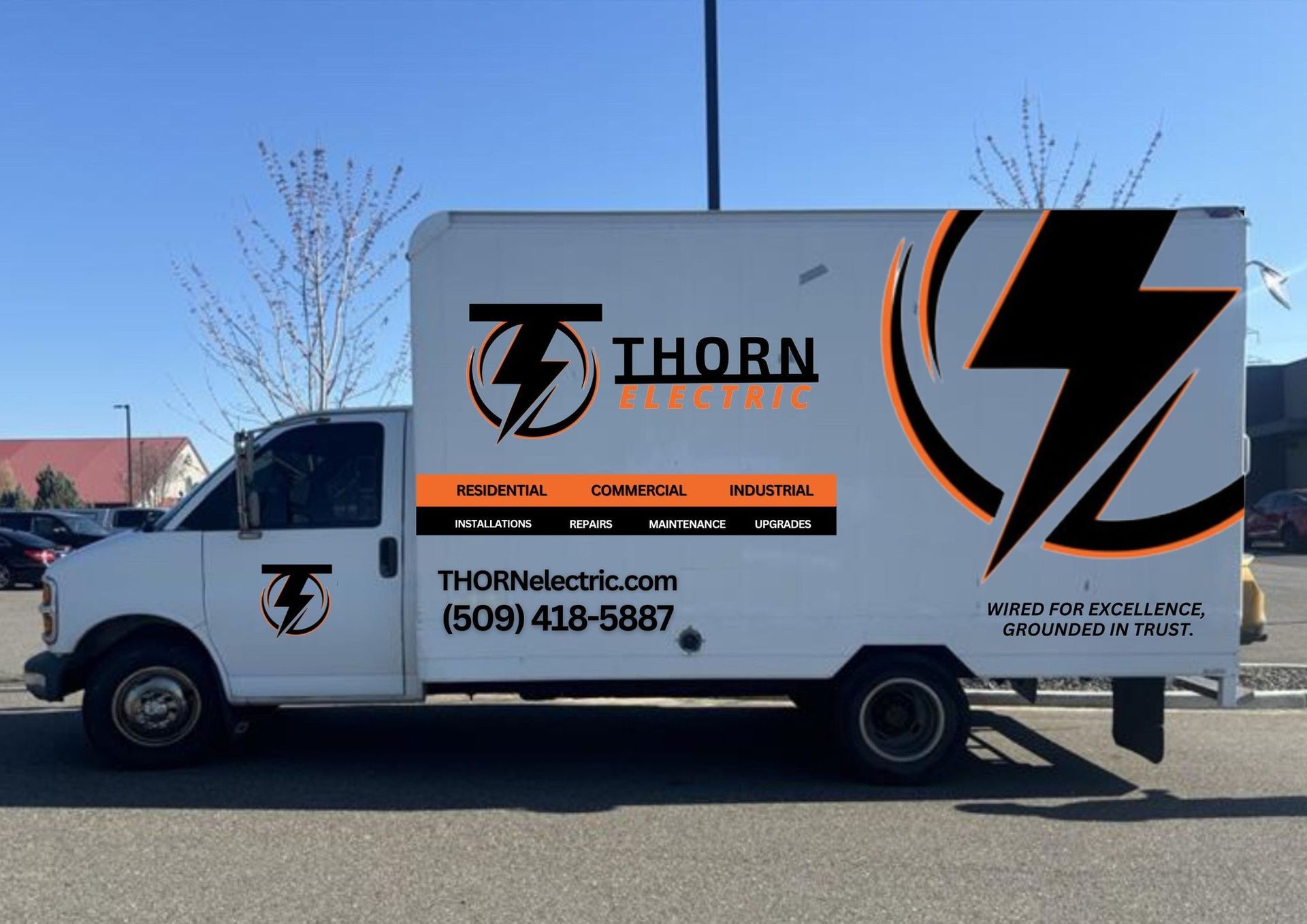 White Thorn Electric truck with black and orange logo, parked in a parking lot with a building in the background.