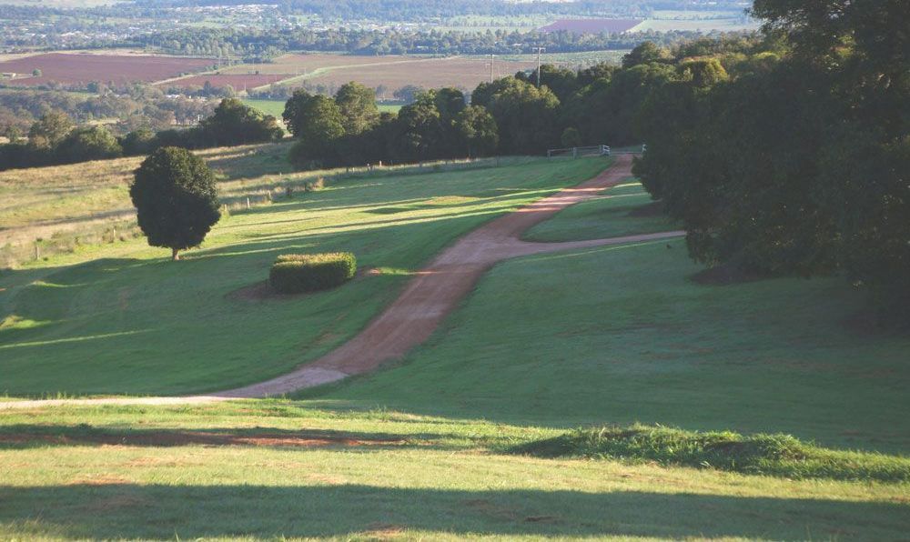 A Dirt Road Going Through A Grassy Field With Trees In The Background — JJ's Excavator & Tipper Hire in Kingaroy, QLD