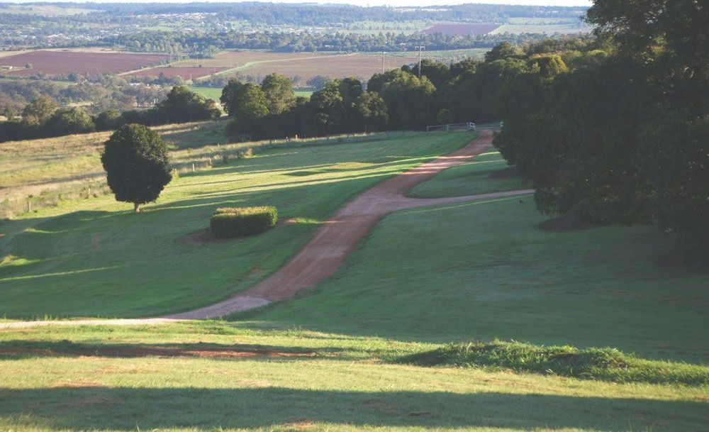A Dirt Road Going Through A Grassy Field With Trees In The Background — JJ's Excavator & Tipper Hire in Kingaroy, QLD