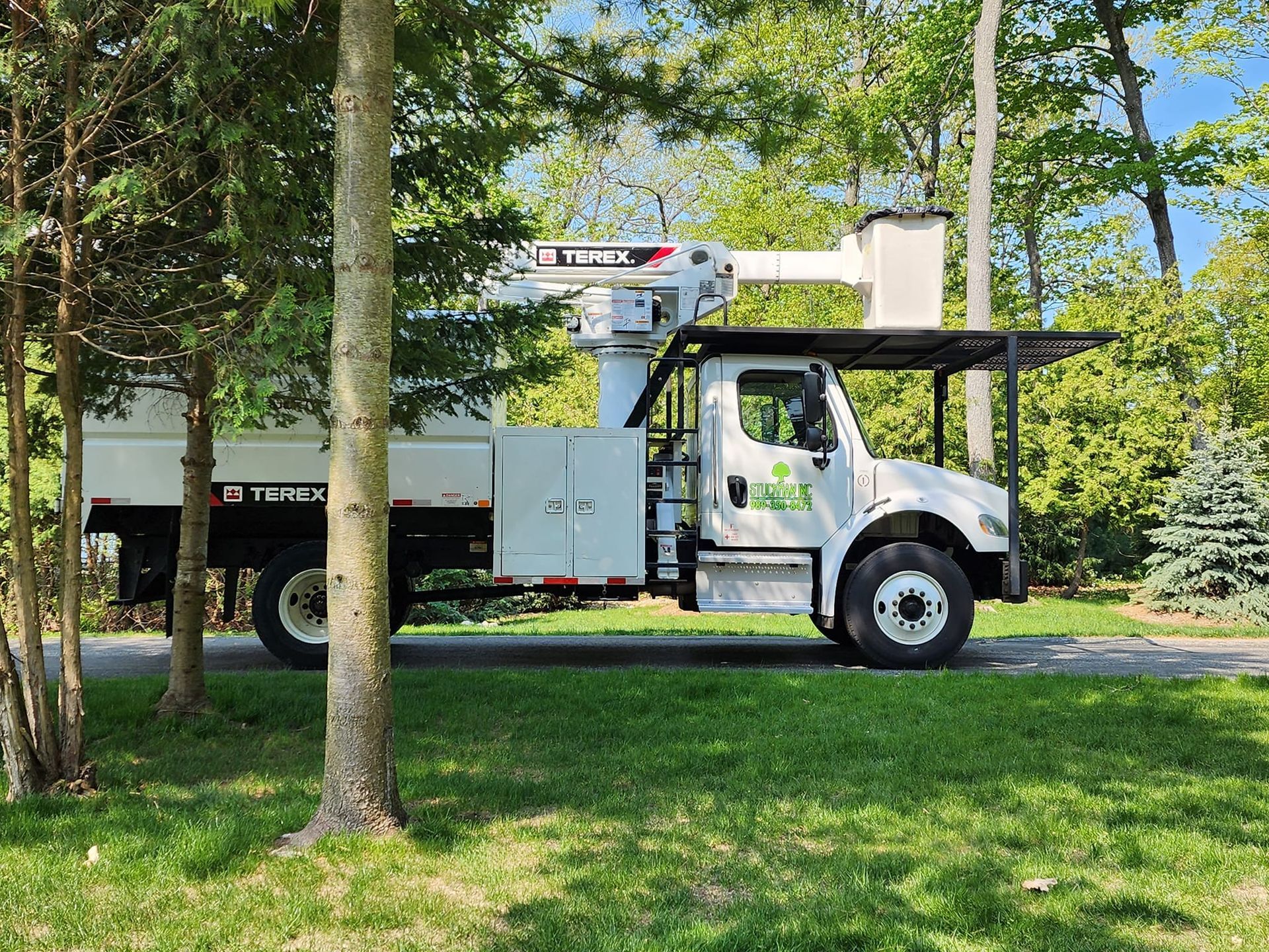 A white truck with a crane on top of it is parked next to a tree.