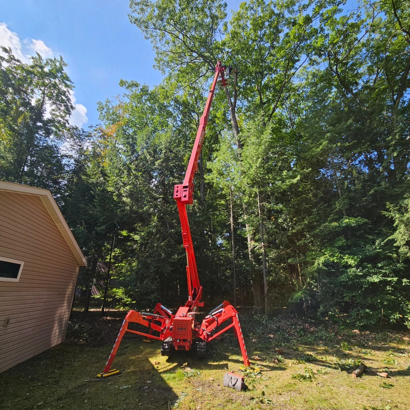 A red crane is cutting a tree in front of a garage - Gaylord, MI - Stuckman Tree Service