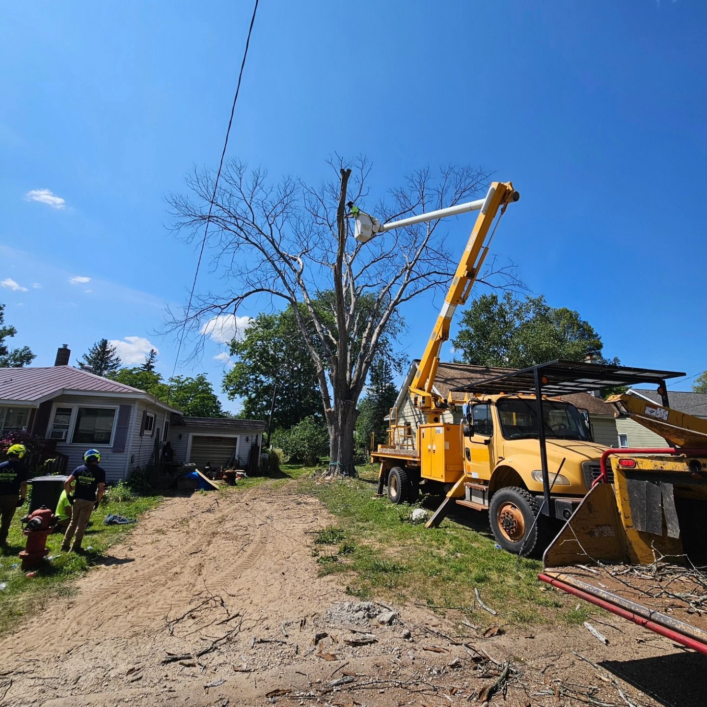 A yellow truck with a crane attached to it is cutting a tree - Gaylord, MI - Stuckman Tree Service