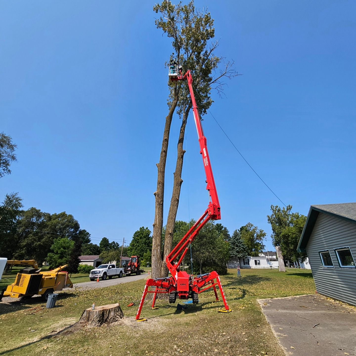 A red crane is cutting down a tree in front of a house - Gaylord, MI - Stuckman Tree Service