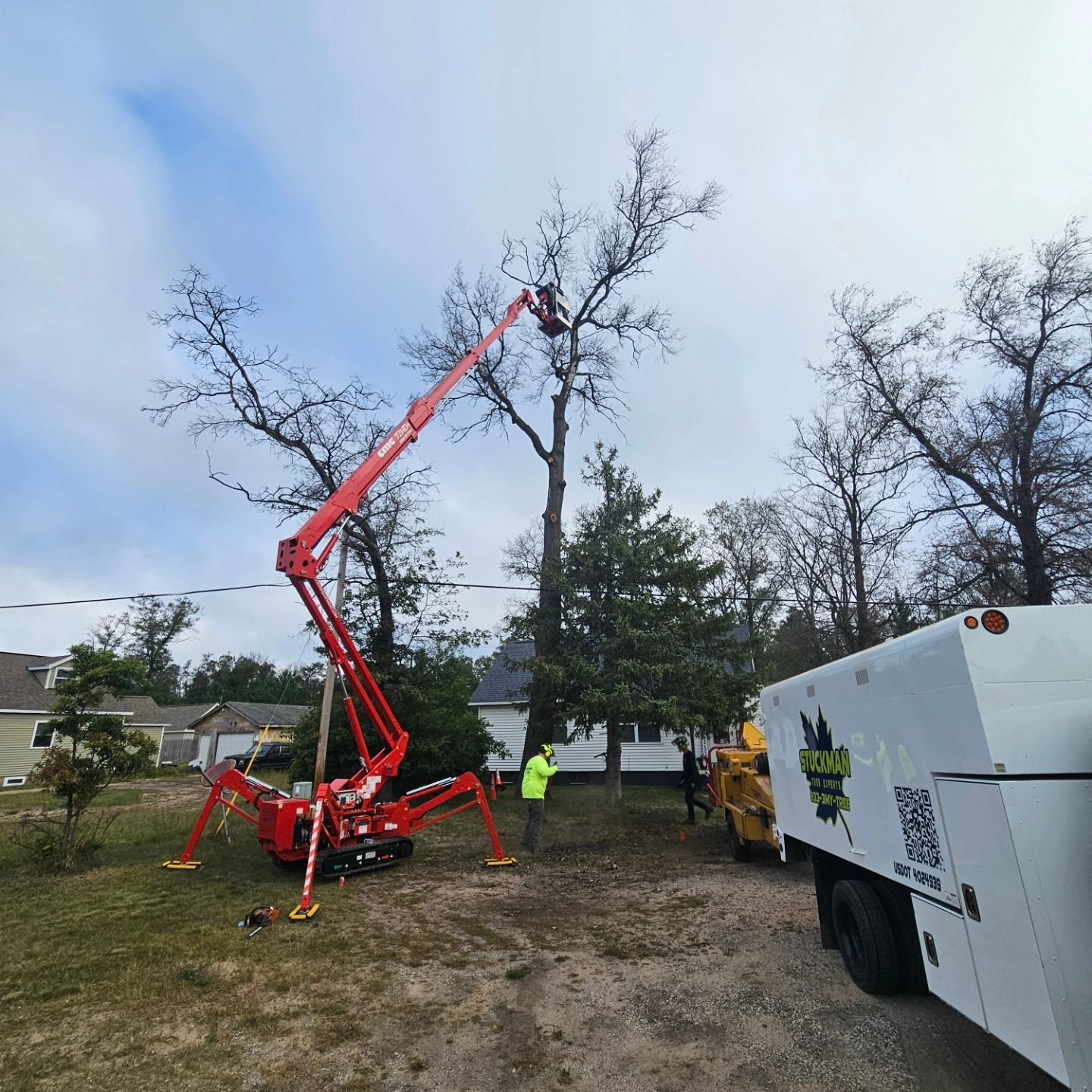 A man is cutting a tree with a crane in a yard - Gaylord, MI - Stuckman Tree Service