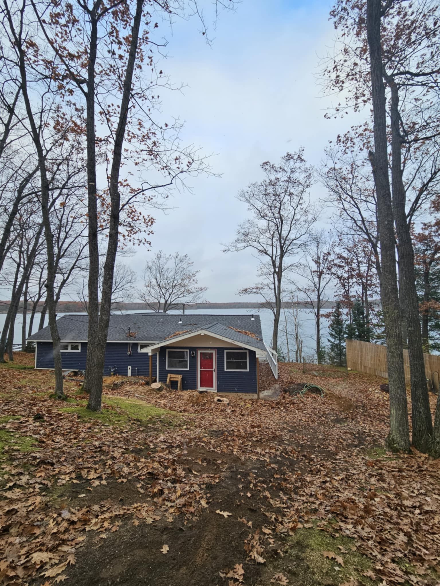 A blue house with a red door is surrounded by trees and leaves.