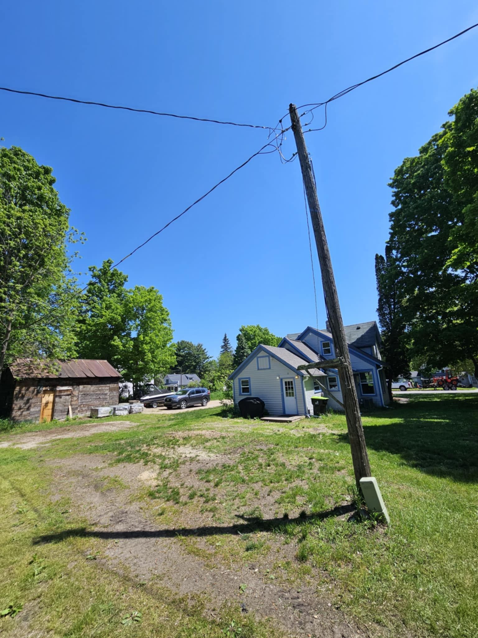 A telephone pole is sitting in the middle of a grassy field in front of a house.