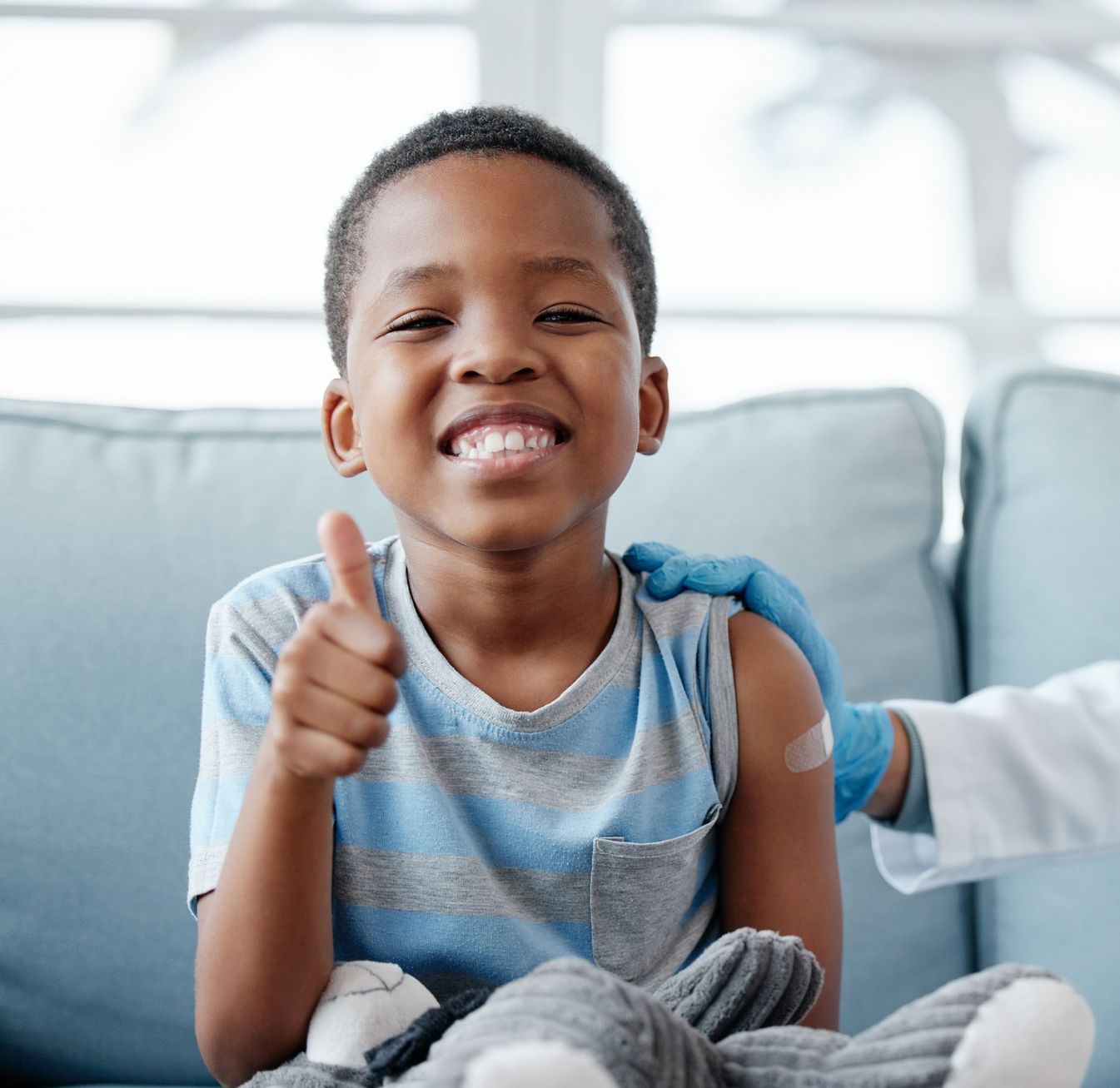 Medical professional  giving pediatric care to a young boy who is giving a thumbs up and smiling.