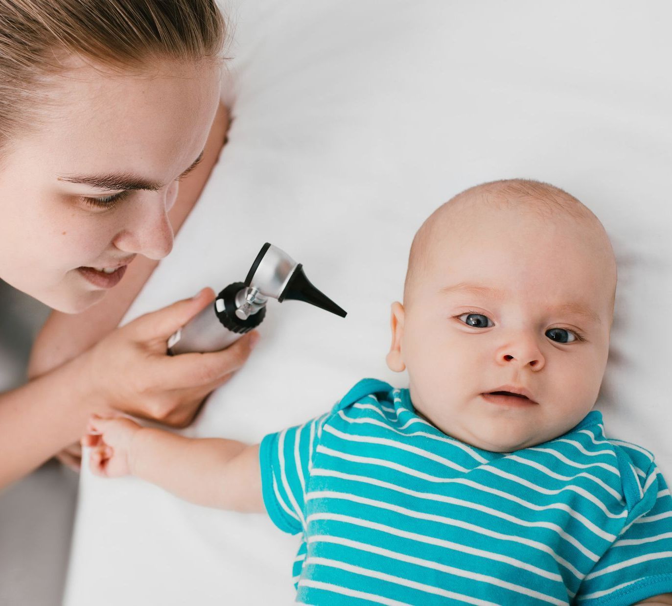 Medical professional  giving pediatric care by checking the ears of a young baby.