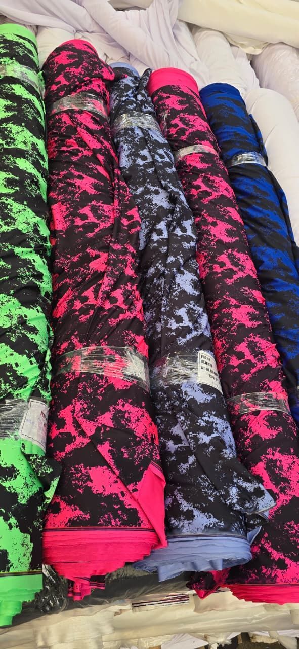 Rollos de tela con patrones de camuflaje digital en varios colores: verde, rosa, azul y negro.