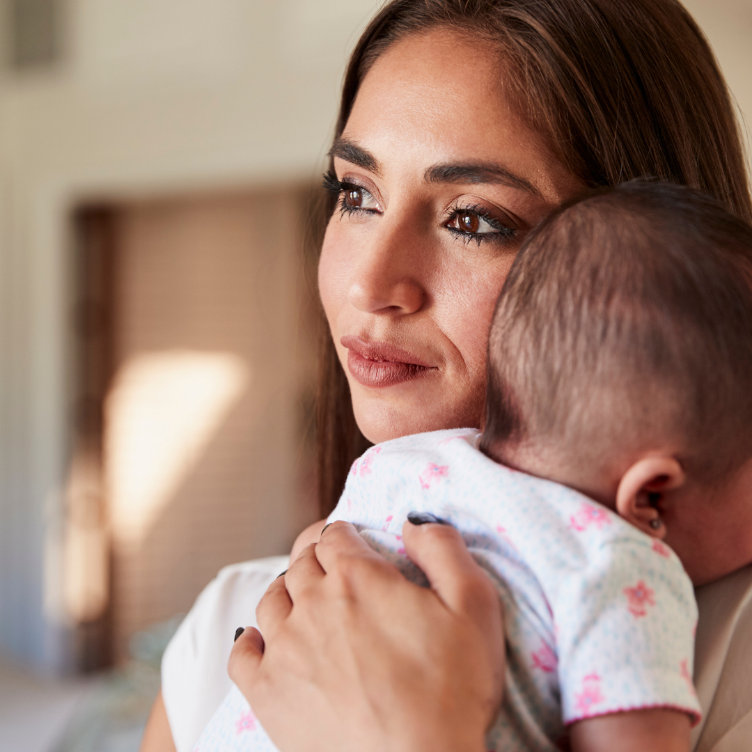 Baby smiling while breastfeeding. Light blue onesie, white blanket, tan skin, indoor setting.