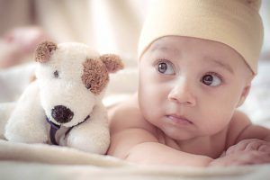 Baby smiling while breastfeeding. Light blue onesie, white blanket, tan skin, indoor setting.