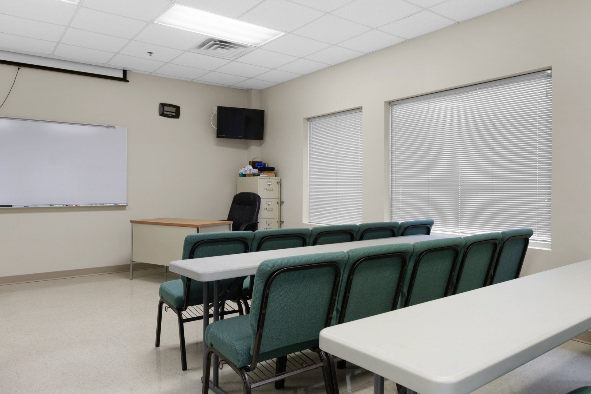 Classroom with rows of chairs, desks, whiteboard, windows, and TV.