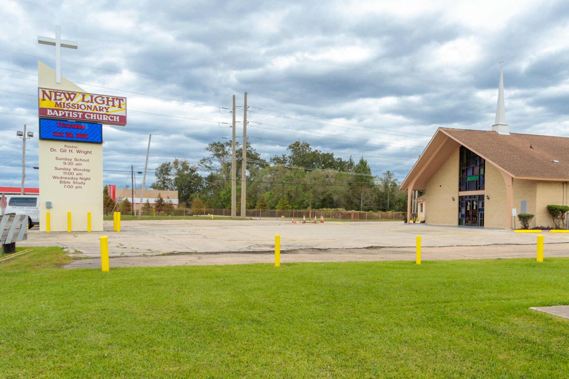 New Light Ministries church with a sign, overcast sky. Empty lot, yellow bollards, green grass.