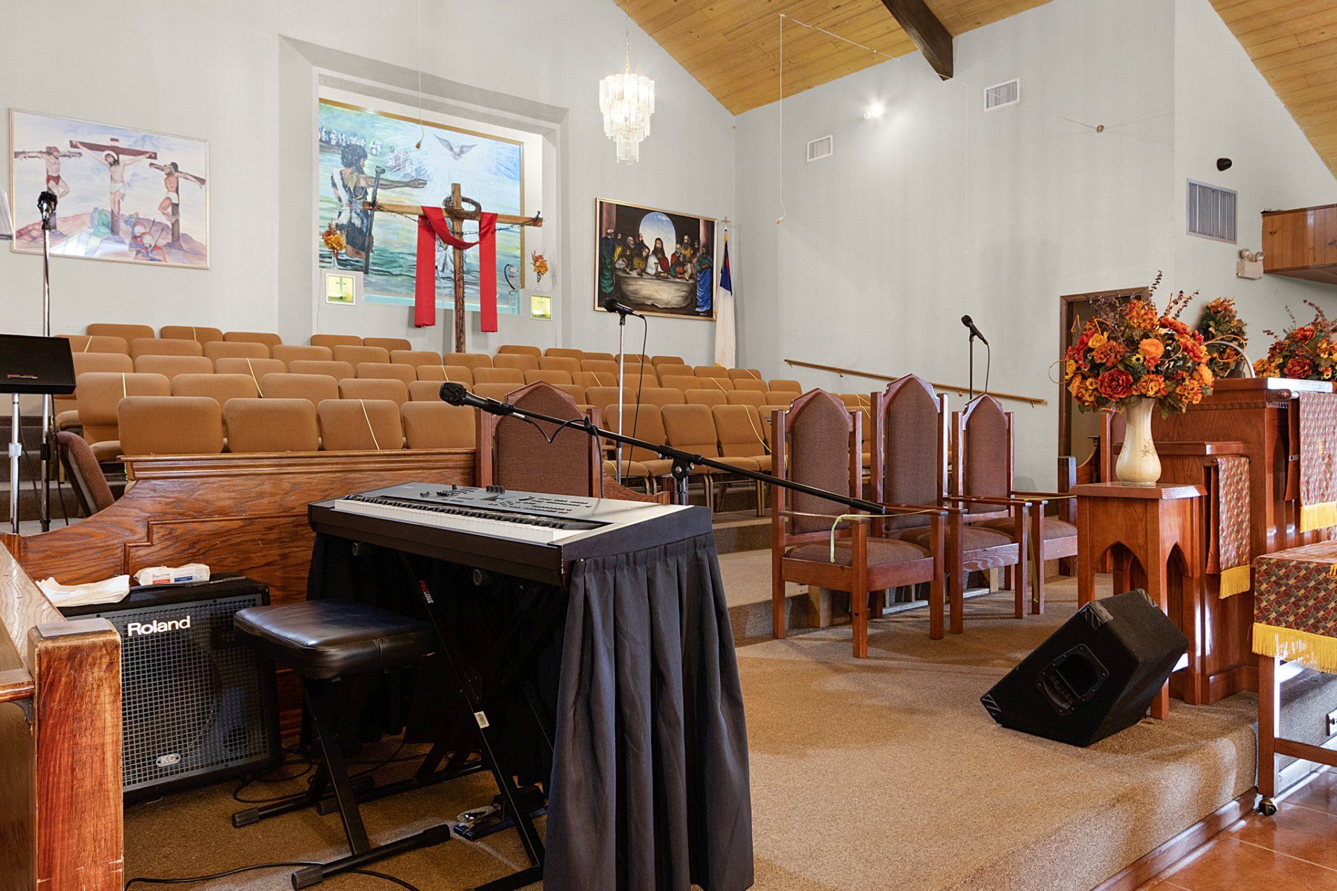 Church interior with a keyboard, rows of pews, and religious artwork on the walls.