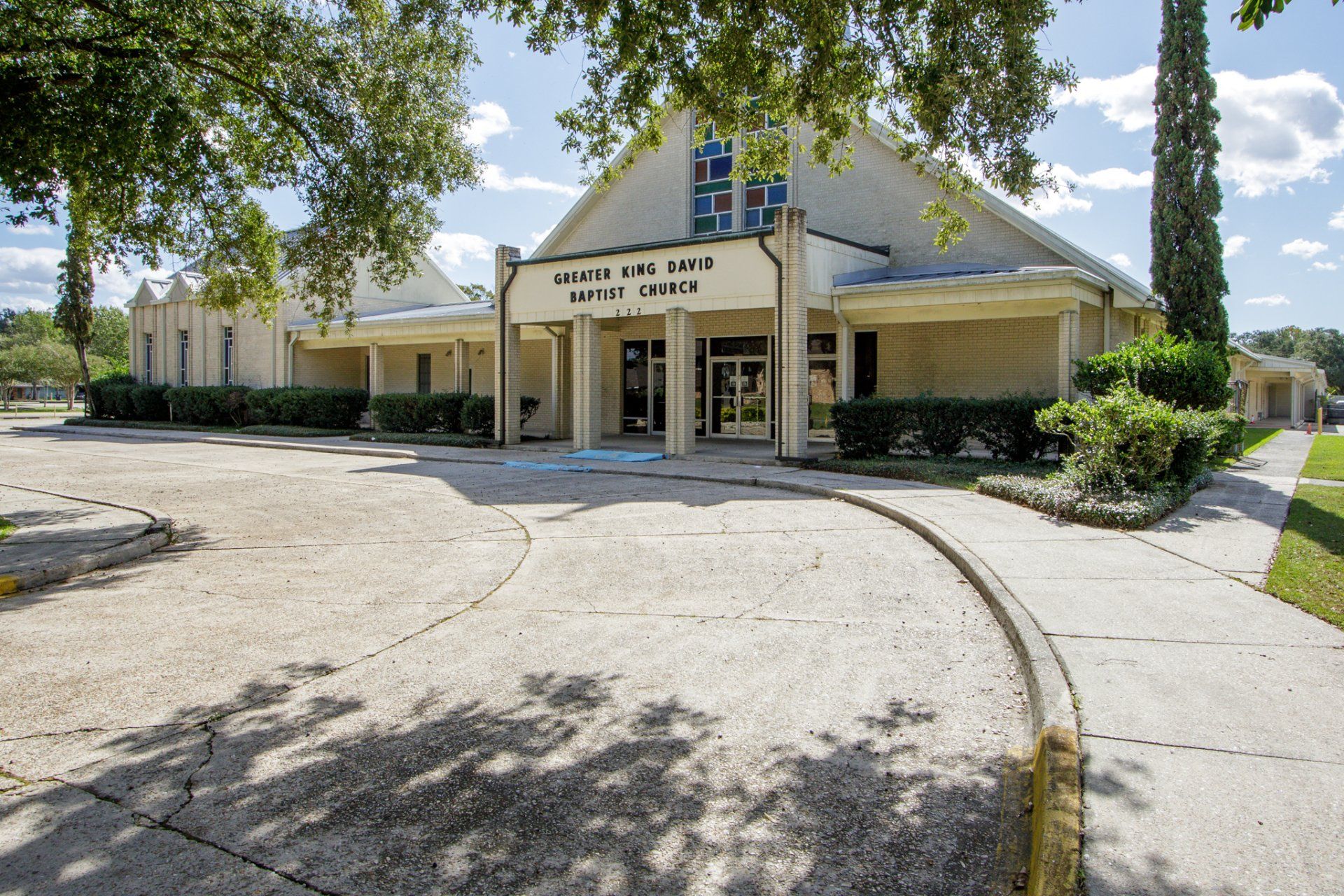 Church building with beige facade, arched roof, and landscaped lawn.