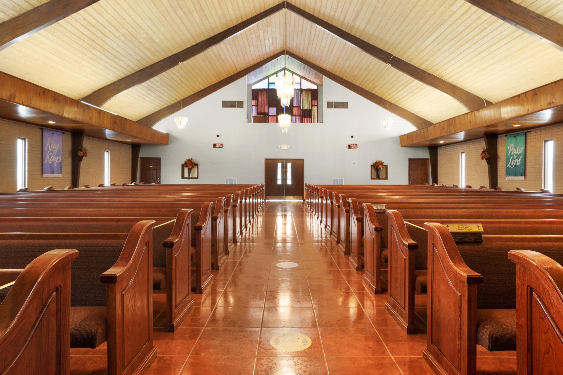 Interior view of a church with rows of wooden pews, a bright central aisle, and a high, wooden-beamed ceiling.