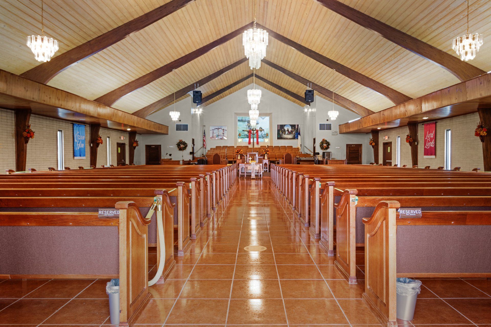 Interior of a church with wooden pews, tiled floor, and chandelier lighting.