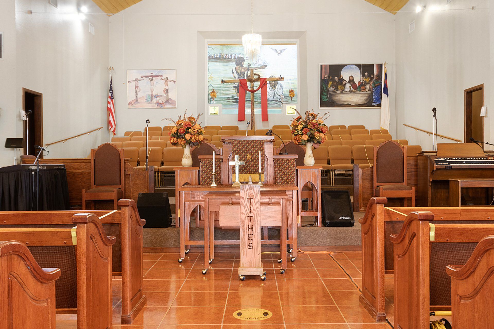Interior of a church with wooden pews, altar, cross, and floral arrangements.