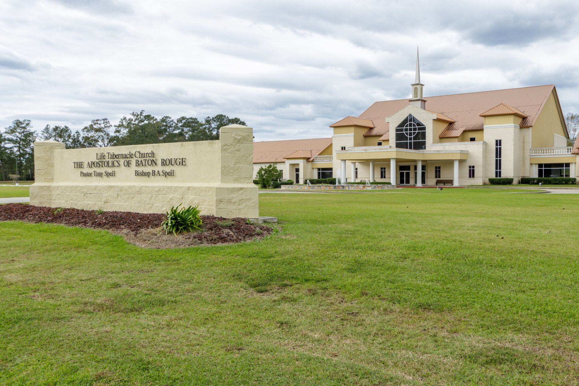 Sign and beige church building under cloudy sky.