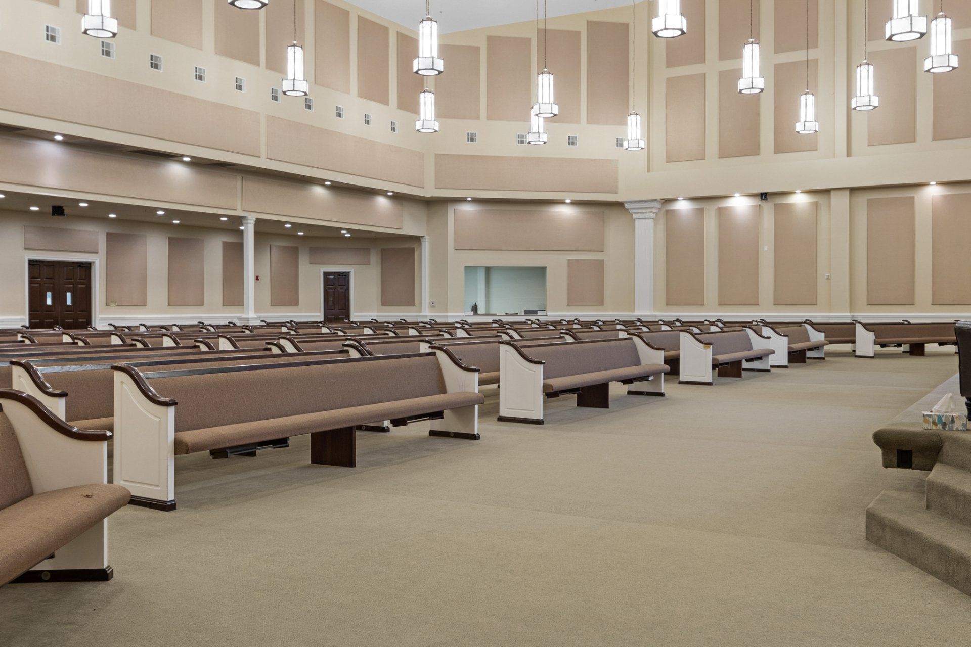 Empty church sanctuary with rows of pews, neutral color palette, and decorative lighting.