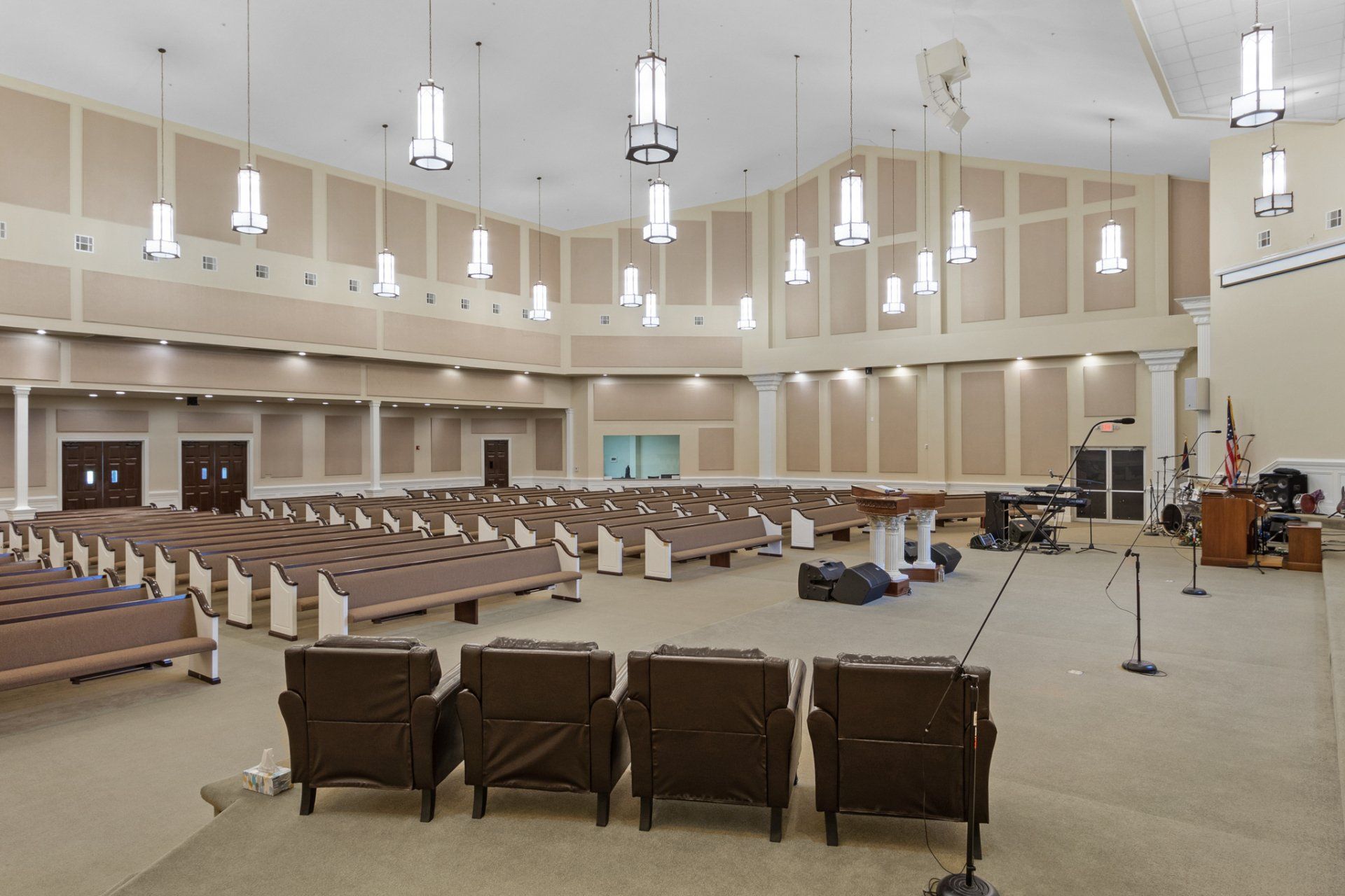 Interior of an empty auditorium with rows of pews, a stage with sound equipment, and hanging lights.