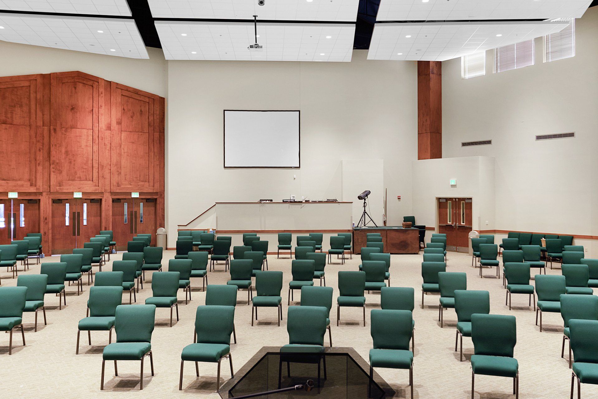 Empty auditorium with rows of green chairs facing a stage with a screen.