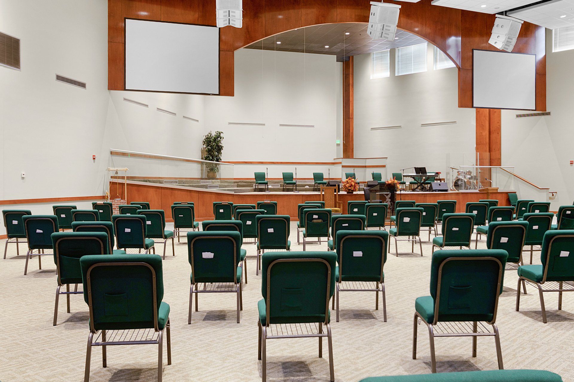Empty church auditorium with green chairs arranged for a service, stage in the back, and large screens.