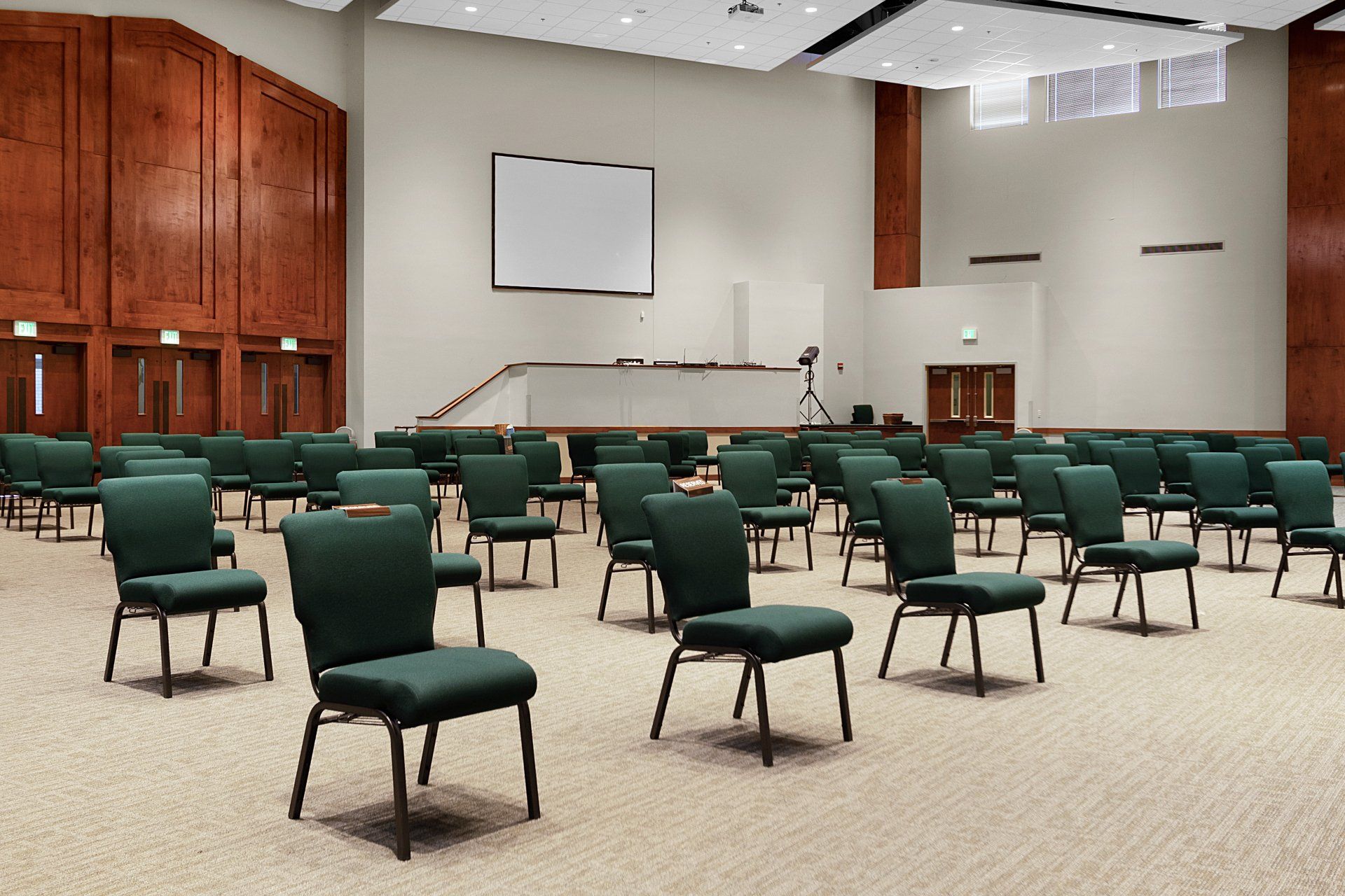 Empty auditorium with rows of green chairs facing a stage with a projector screen.