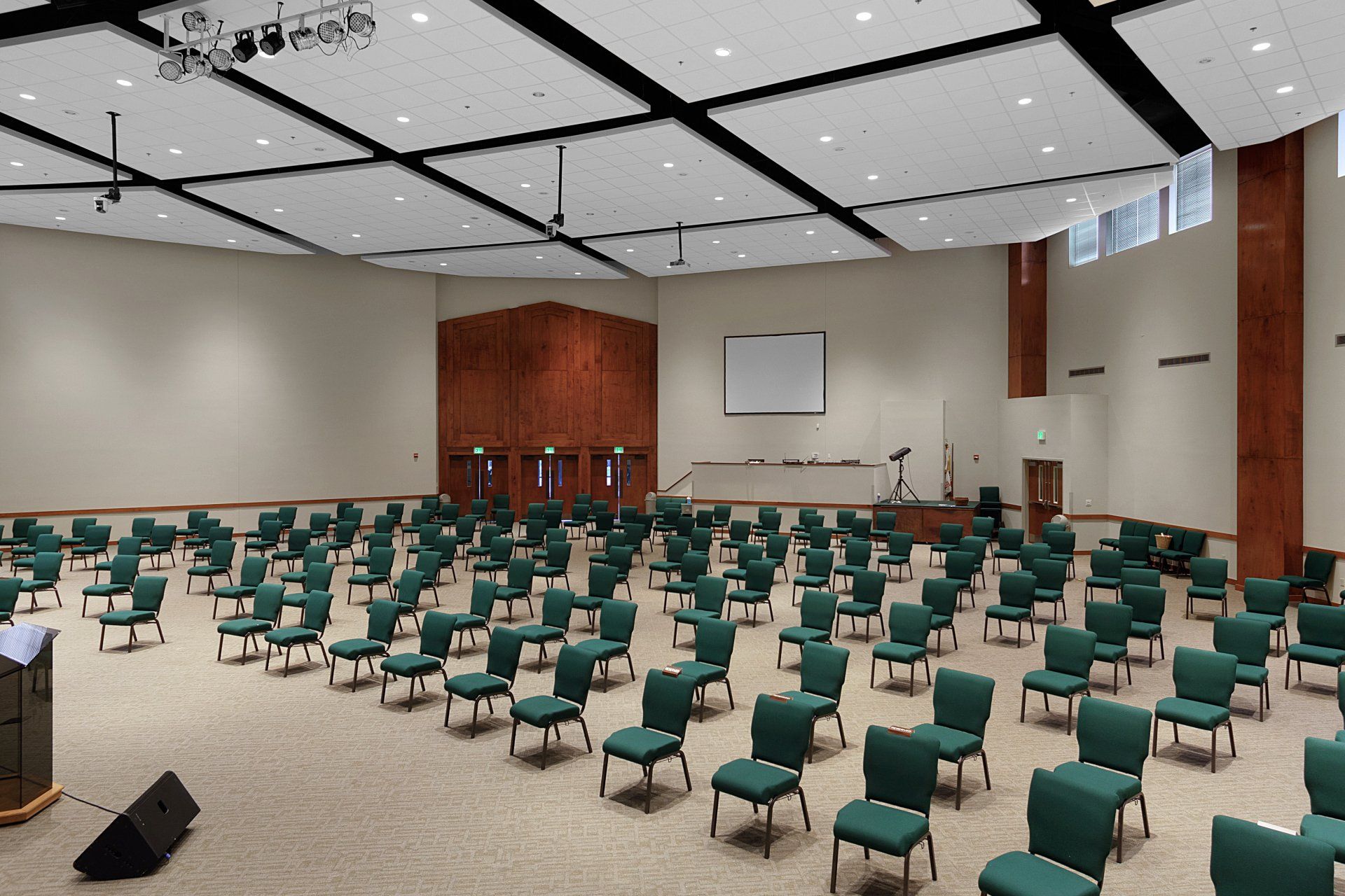 Empty auditorium with rows of green chairs, stage, and projection screen.