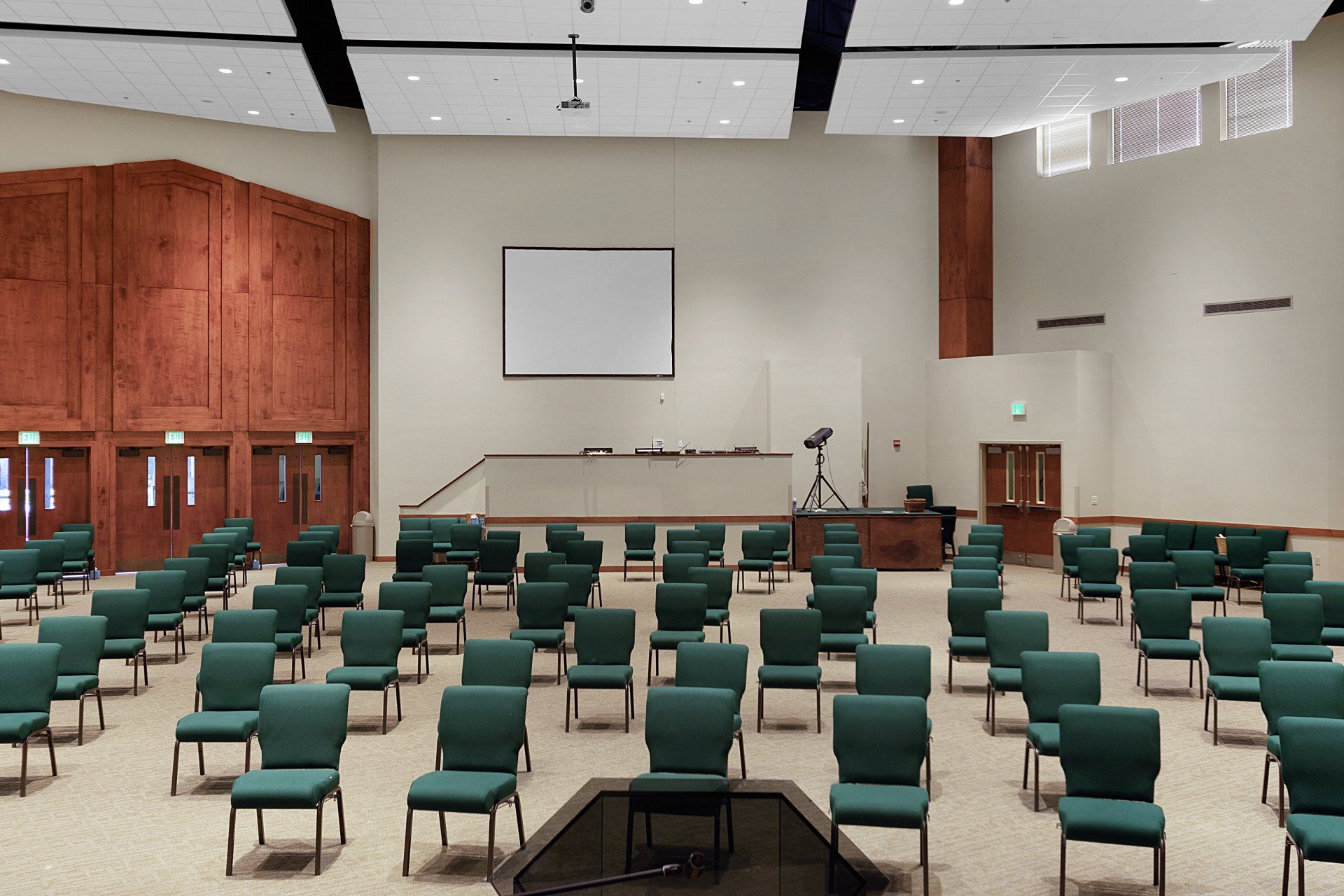 An empty auditorium with rows of green chairs facing a stage with a screen.