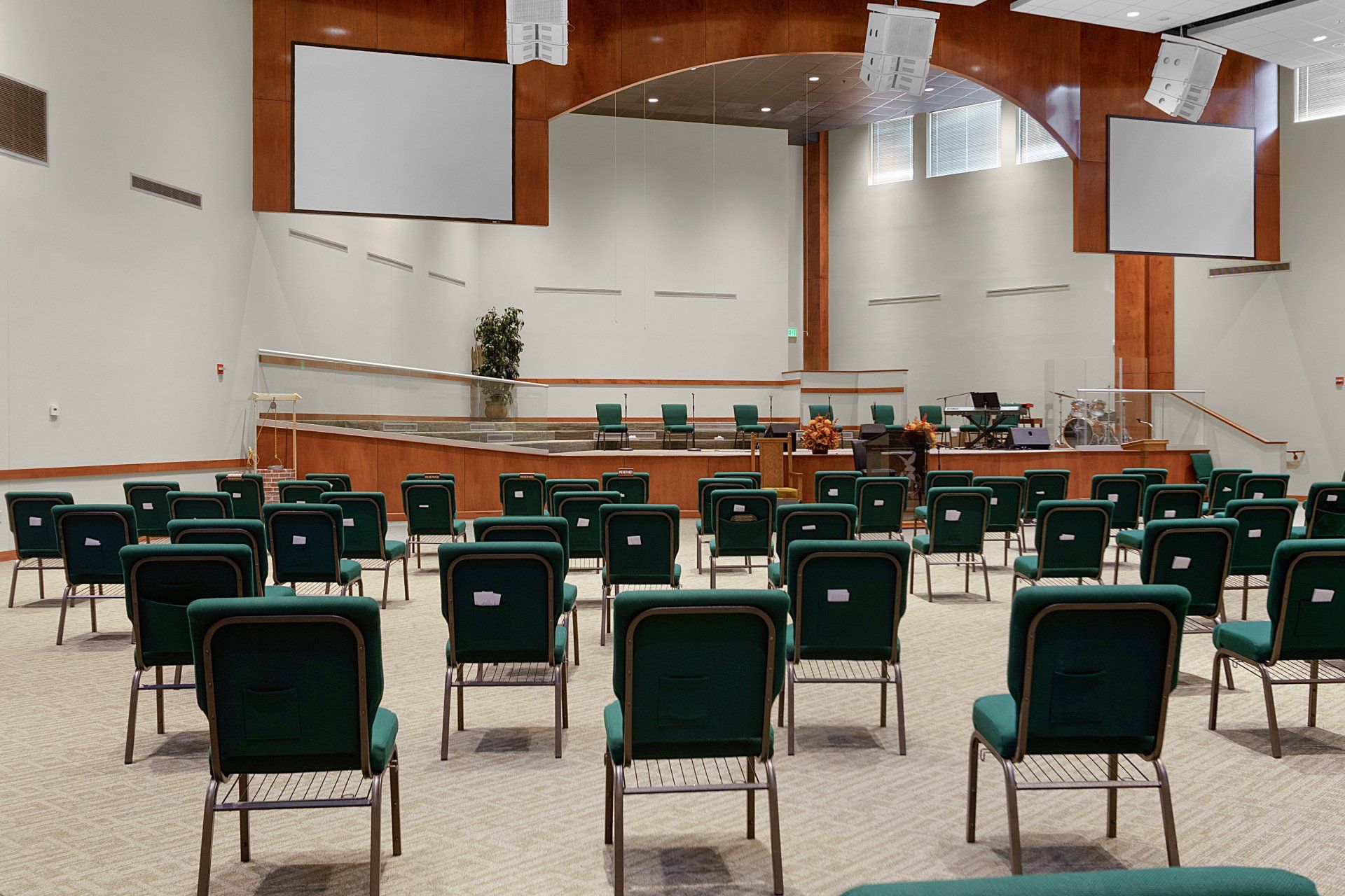 Empty church auditorium with green chairs, stage, screens, and wooden accents.